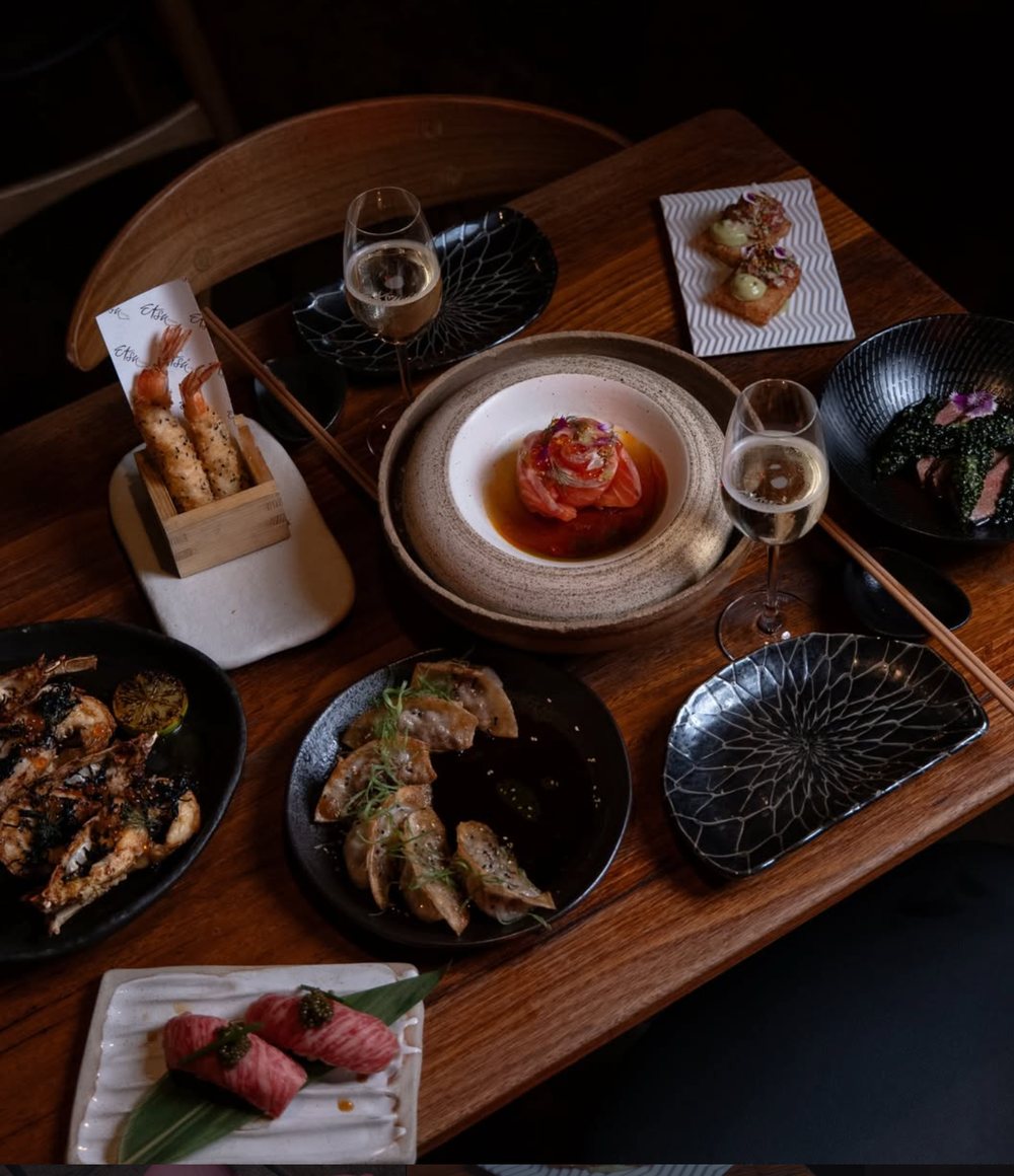 Japanese dishes, sake and wine spread across a dark timber table at Etsu Izakaya