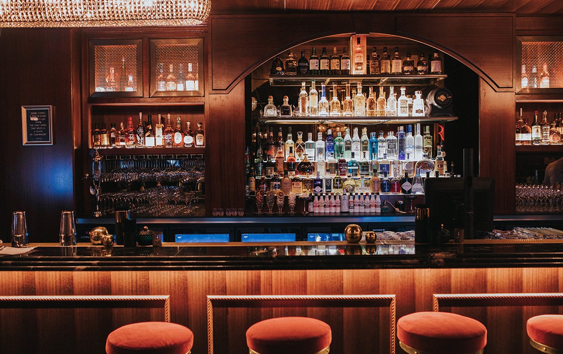 The backlit bar and red velvet stools at The Roosevelt Lounge