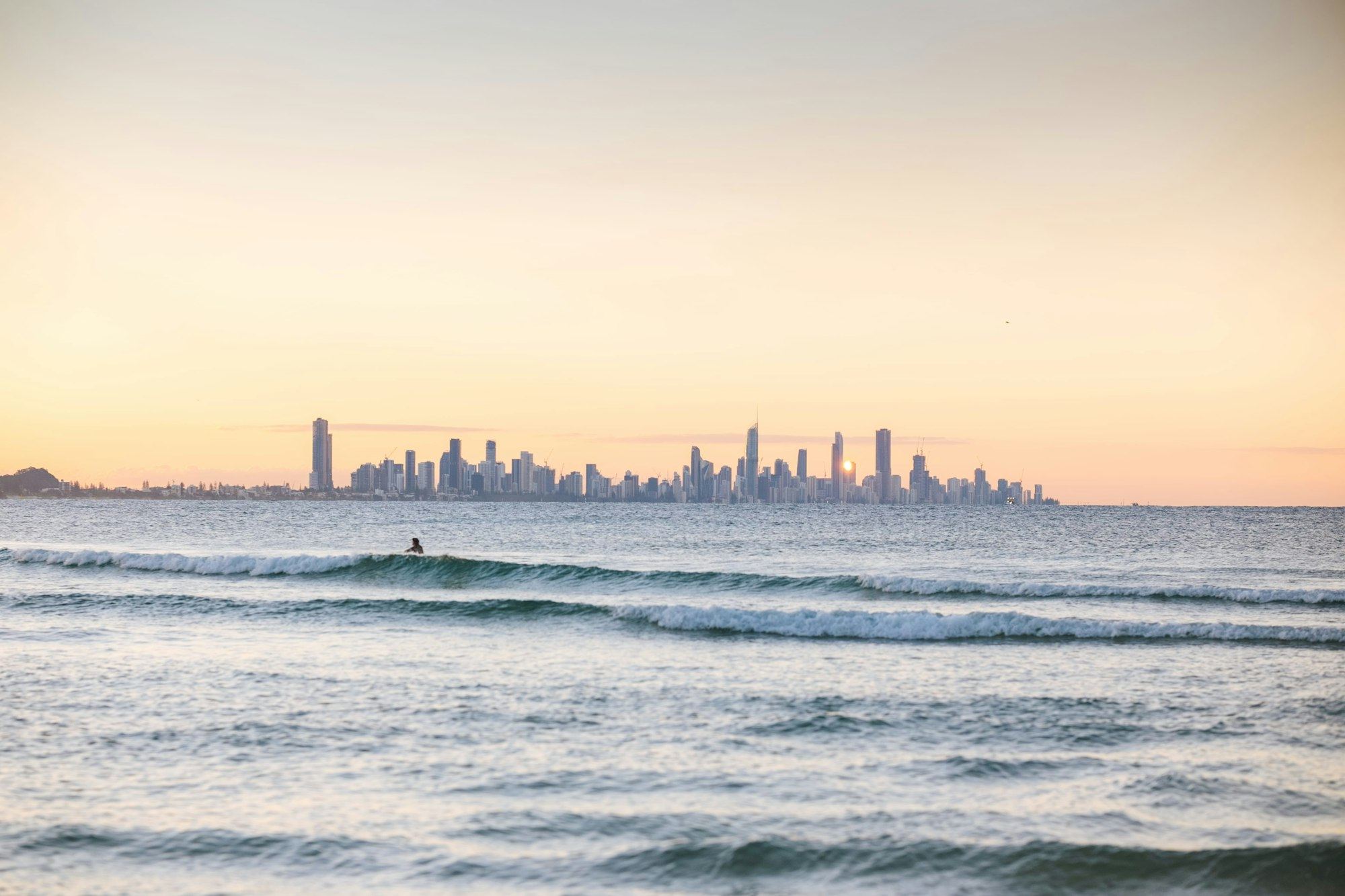 A lone surfer at Currumbin Alley at golden hour, with the Gold Coast skyline on the horizon