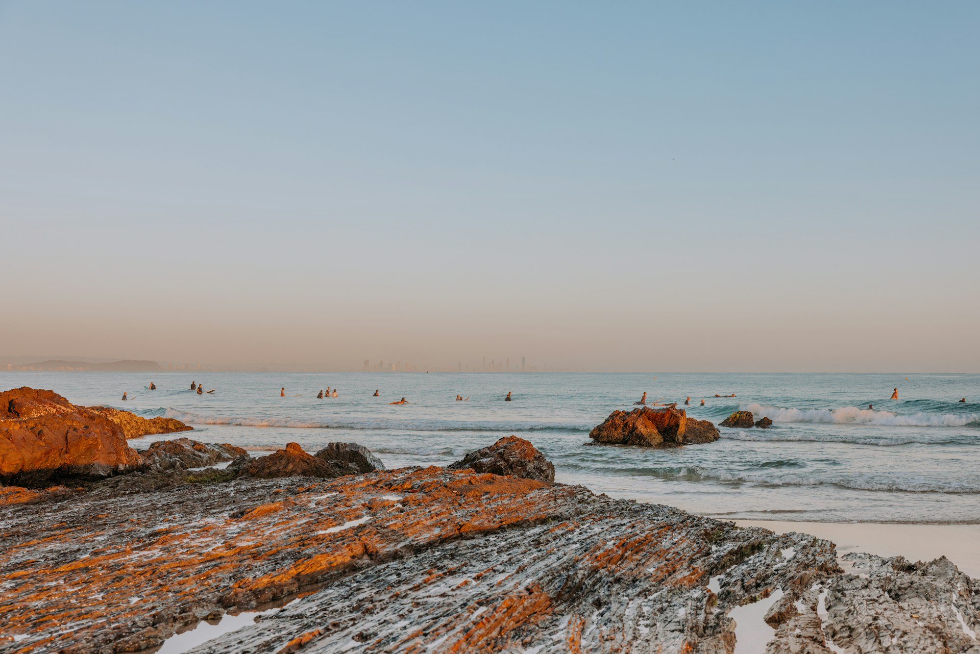 Early-morning swimmers beyond the rocks on a calm, pastel sea