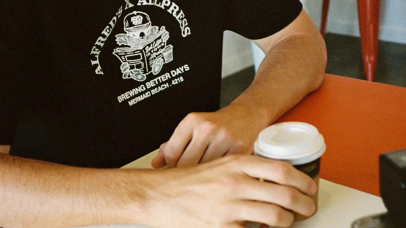 A barista in an Alfred's Apartment T-shirt with a takeaway coffee
