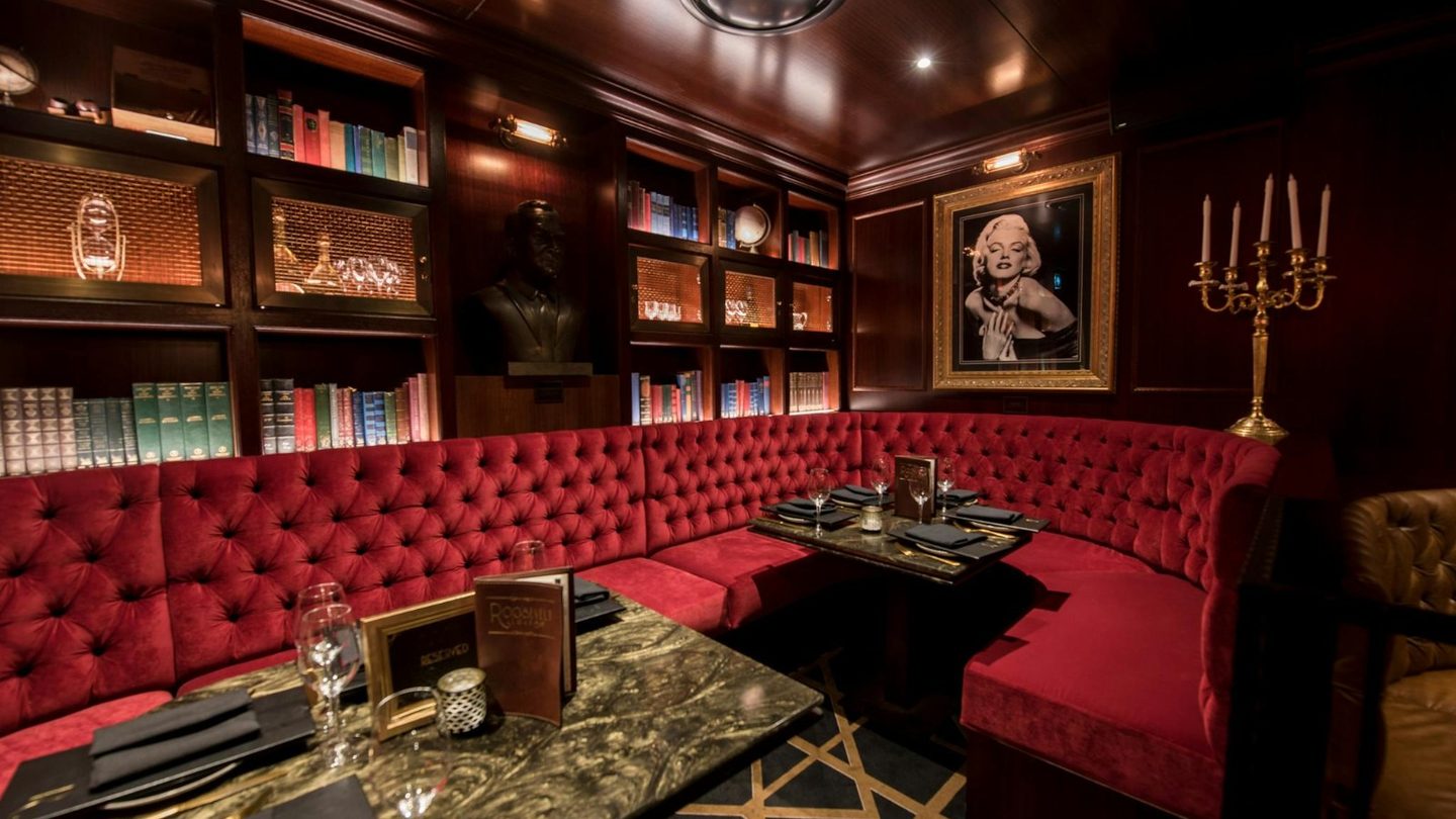 A red velvet booth beneath bookshelves at The Roosevelt Lounge