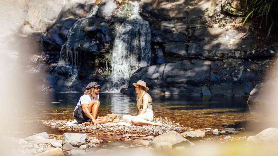 Two walkers sitting beside the waterfall at Cougal Cascades