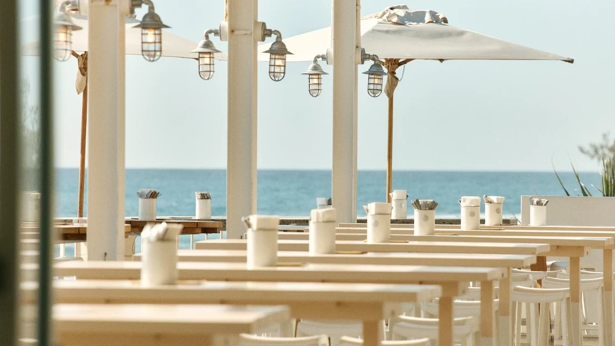 Timber tables under lanterns and umbrellas with the ocean behind, at Burleigh Pavilion