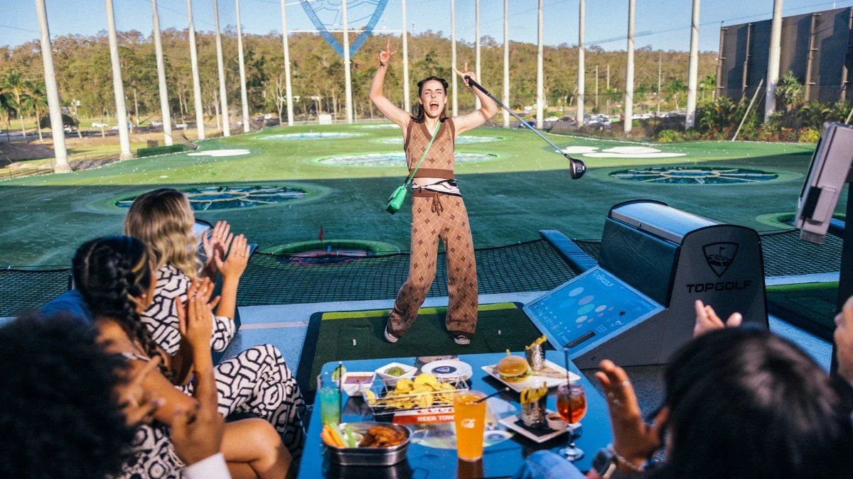 A player swinging in a Topgolf bay while friends cheer