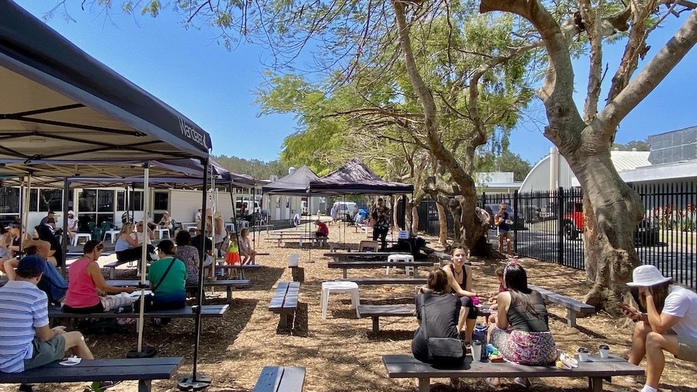Shoppers at tables under the trees at the Palm Beach Farmers Market