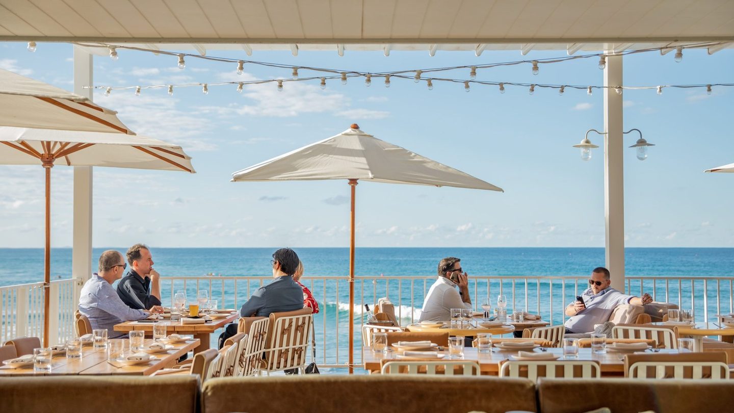 Diners on The Tropic's deck under white umbrellas, looking out to sea