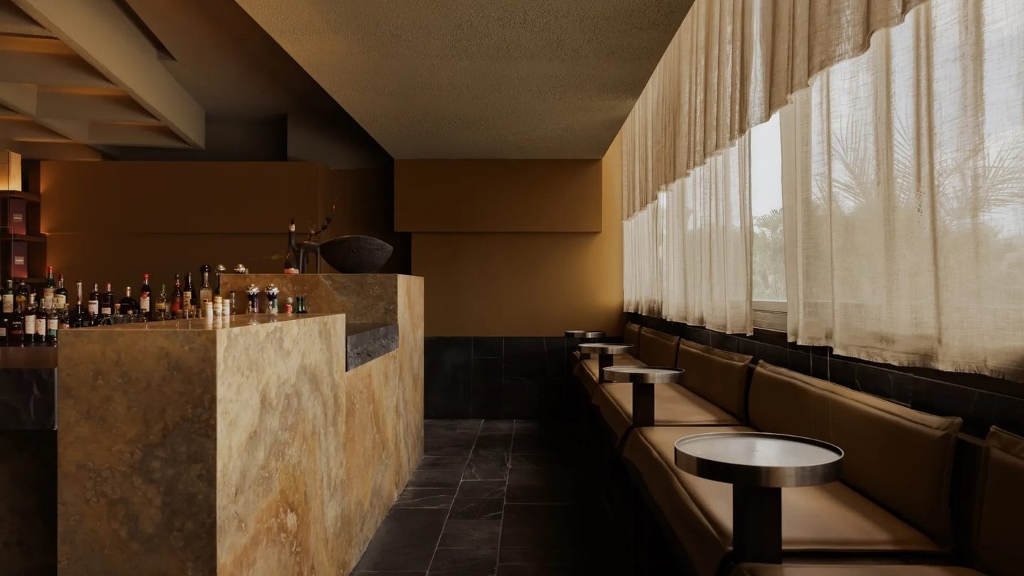 The bar and long banquette inside Norté, with sheer curtains along the windows