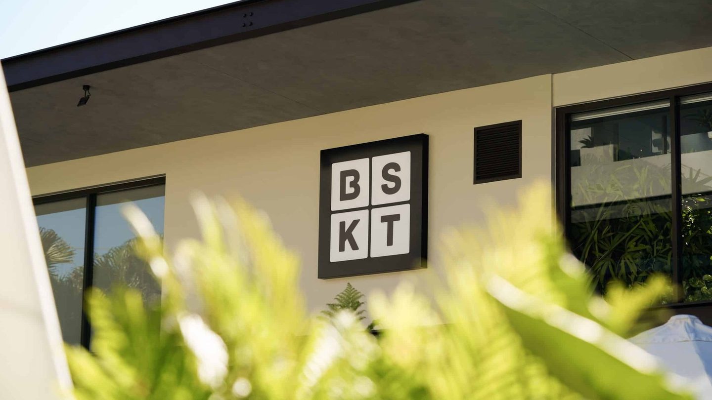 The BSKT Cafe sign on the building, behind leafy plants