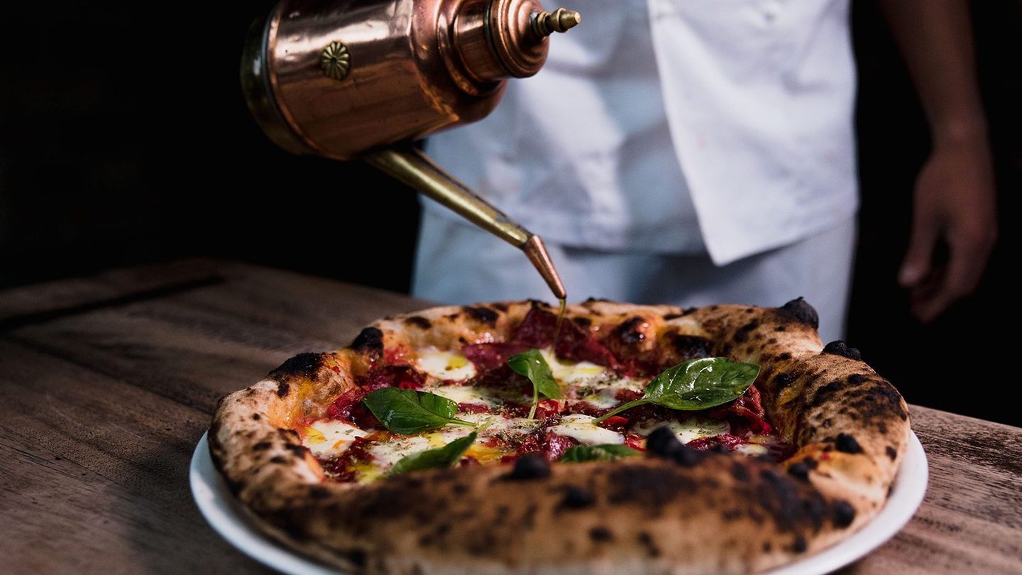 Oil being poured over a wood-fired pizza at Gemelli Italian