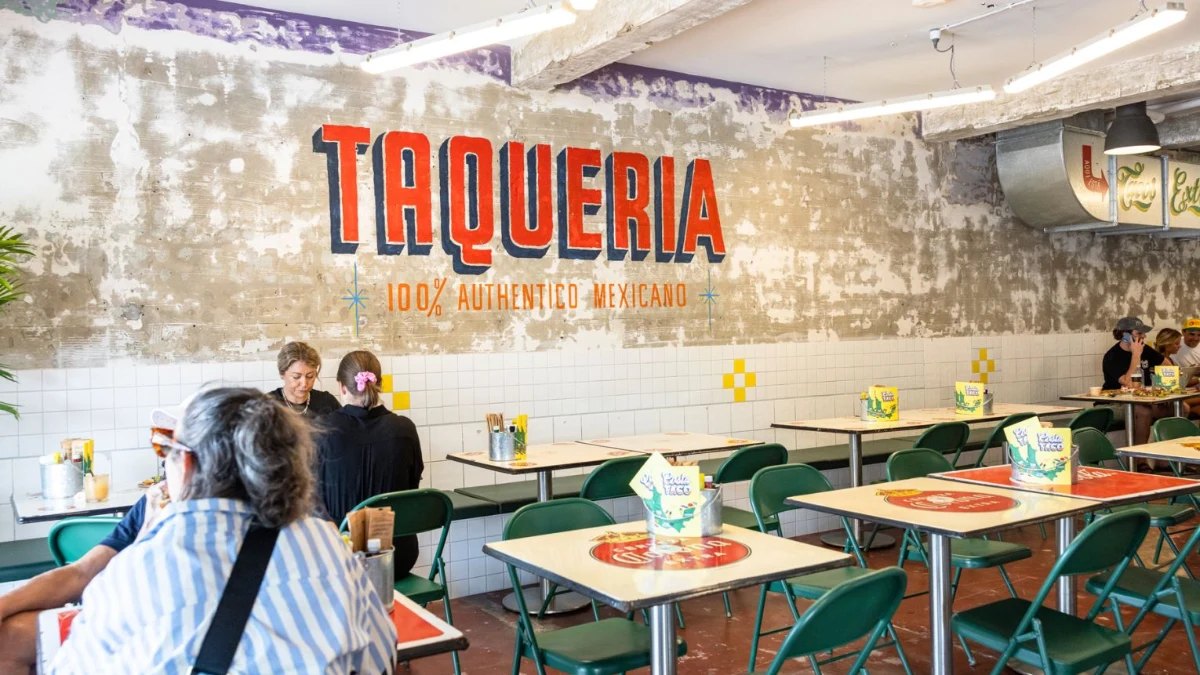 Inside Costa Taco: the Taqueria sign above green chairs