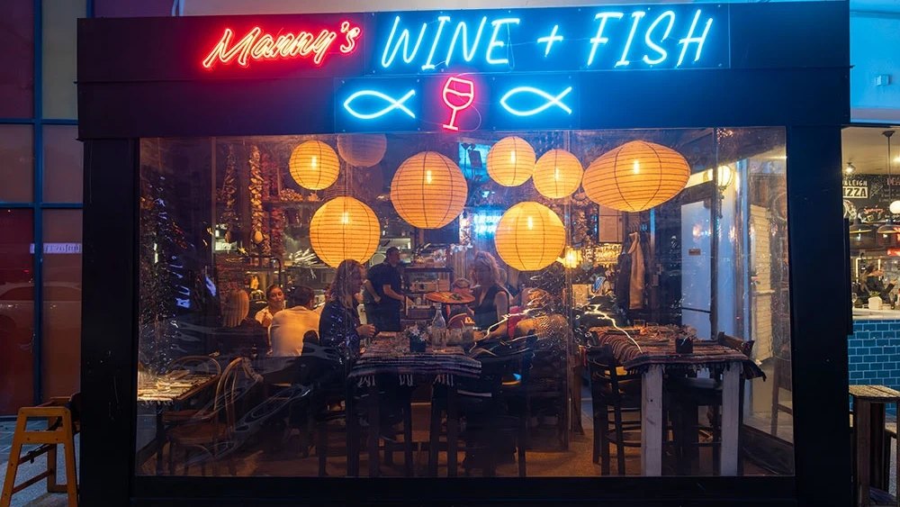 The Wine + Fish neon sign above a window full of paper lanterns at Manny's