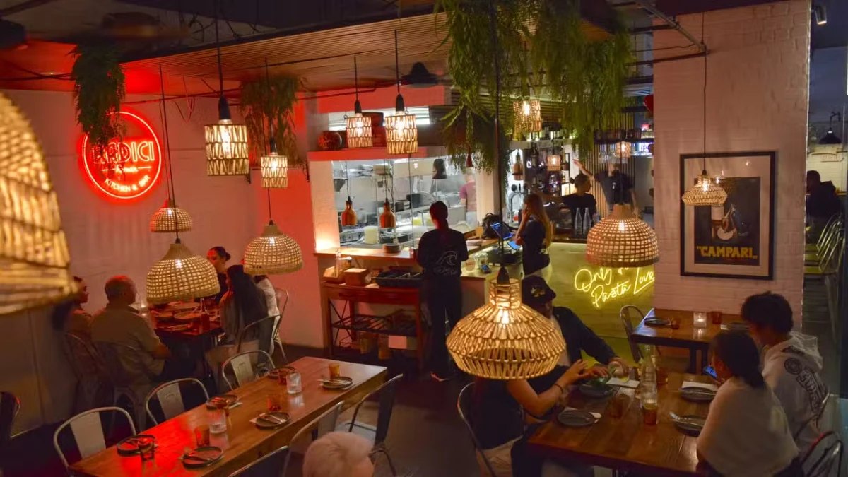 Red neon and woven pendant lights over diners at Radici