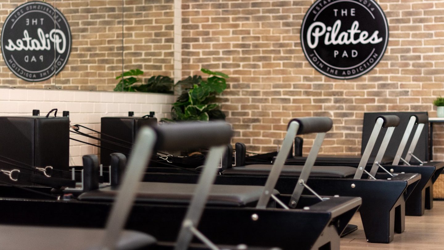 Reformer machines in front of The Pilates Pad's brick wall and logo